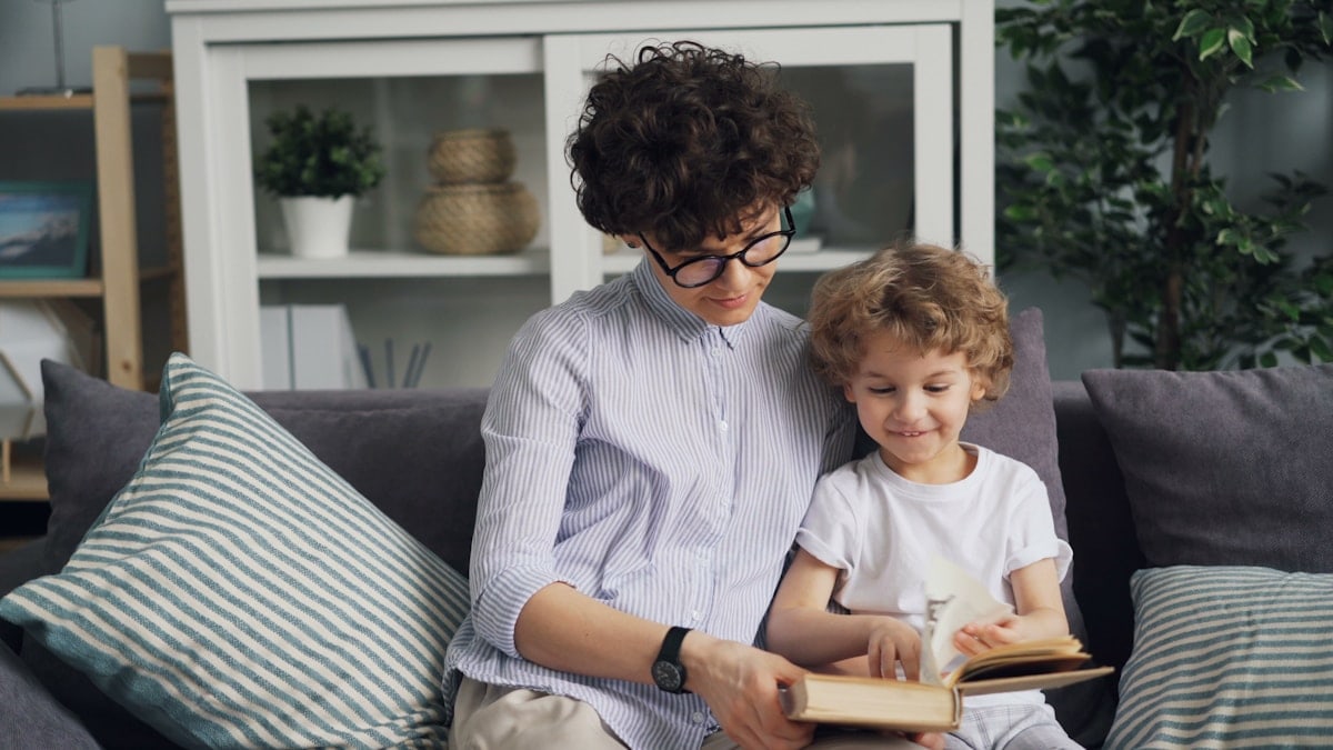 a woman sitting on a couch reading a book to a child